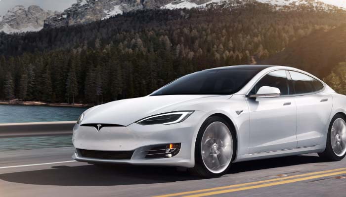 A photo of a Tesla Model S, driving on road next to a lake and forest